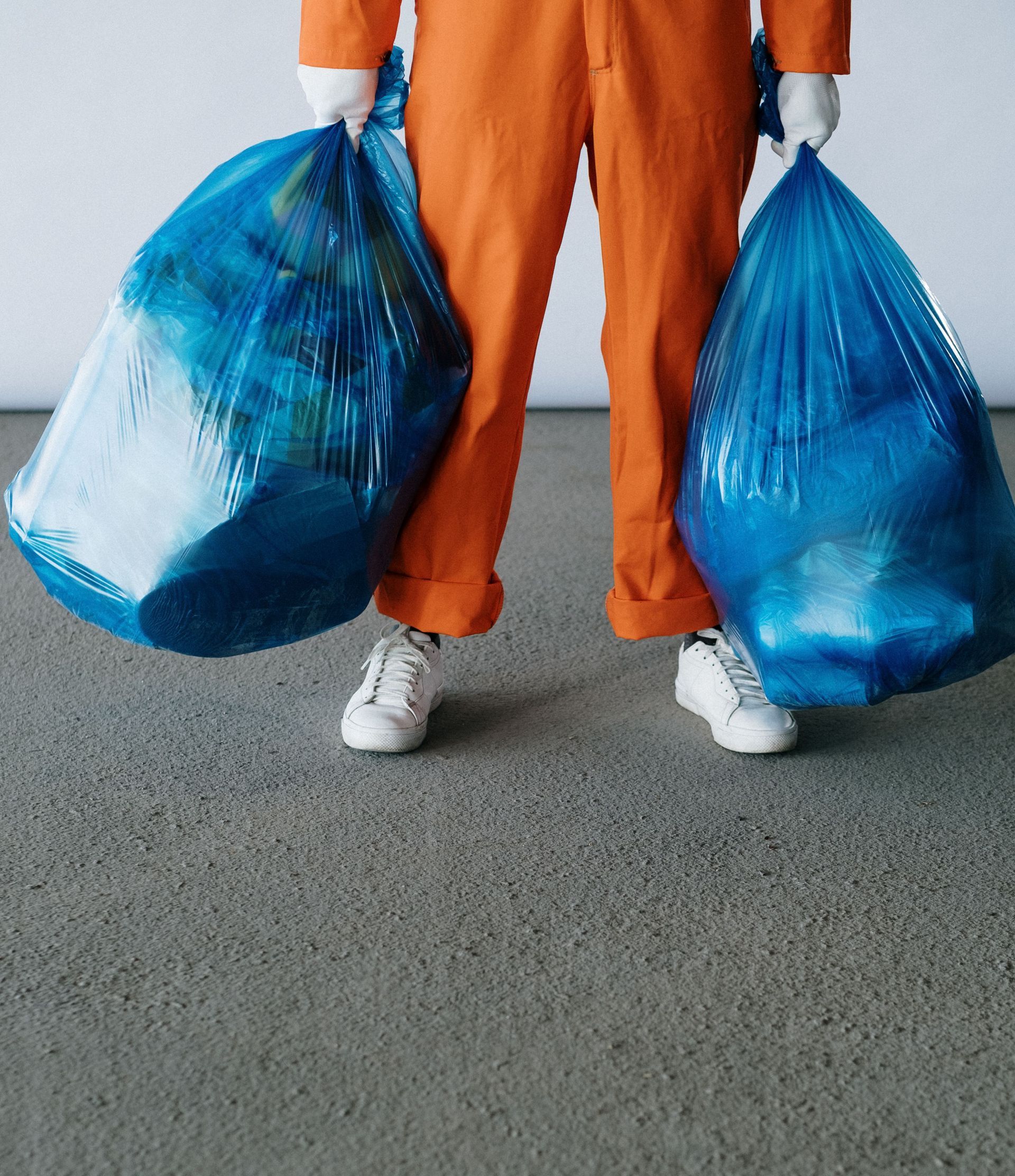 Person in orange uniform holding blue trash bags. Indoor setting focuses on waste management.